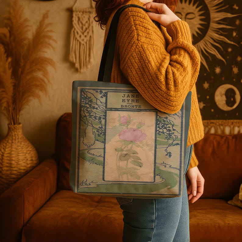 May include: A rectangular tote bag featuring a printed book cover design for Jane Eyre by Bronte. The graphic includes a central illustration of a pink rose, surrounded by a landscape scene with trees and a winding path in muted green and blue tones.