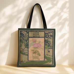 May include: A dark green tote bag with black shoulder straps featuring a rectangular graphic print. The design displays the text JANE EYRE BRONTE above a central illustration of a pink rose on a beige background, surrounded by a dark green landscape.