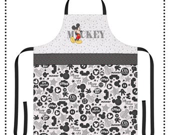 May include: Black and white kitchen apron with a Mickey Mouse design. The apron has a black and white polka dot pattern on the top and a Mickey Mouse themed pattern on the bottom. The apron has a black adjustable neck strap and two black ties. The text "MICKEY" is printed in black on the top of the apron.