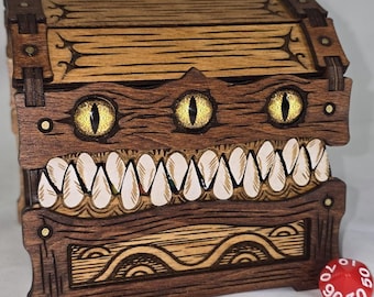 May include: A wooden treasure chest with a monster-like design. The chest features three glowing yellow eyes and a row of white teeth. The chest is brown with decorative wood grain and metal accents. Several dice are scattered around the chest.