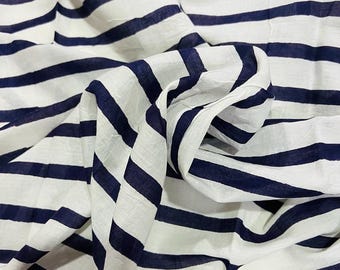 May include: White fabric with navy blue horizontal stripes. The fabric is folded and draped, creating soft shadows and texture. The stripes are evenly spaced and run across the entire width of the material.