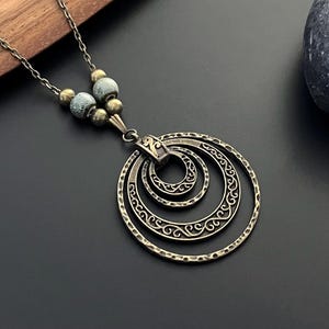 May include: A silver necklace with a layered circle pendant. The circles are textured and have a delicate design. The necklace is accented with small, light blue and silver beads.