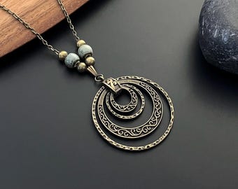 May include: A silver necklace with a layered circle pendant. The circles are textured and have a delicate design. The necklace is accented with small, light blue and silver beads.