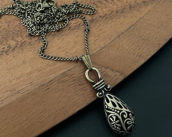 May include: A gold-tone necklace with a detailed teardrop pendant. The pendant has a black enamel finish and intricate floral designs.