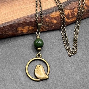 May include: A bronze necklace with a green bead and a pendant featuring a small bird inside a circle.