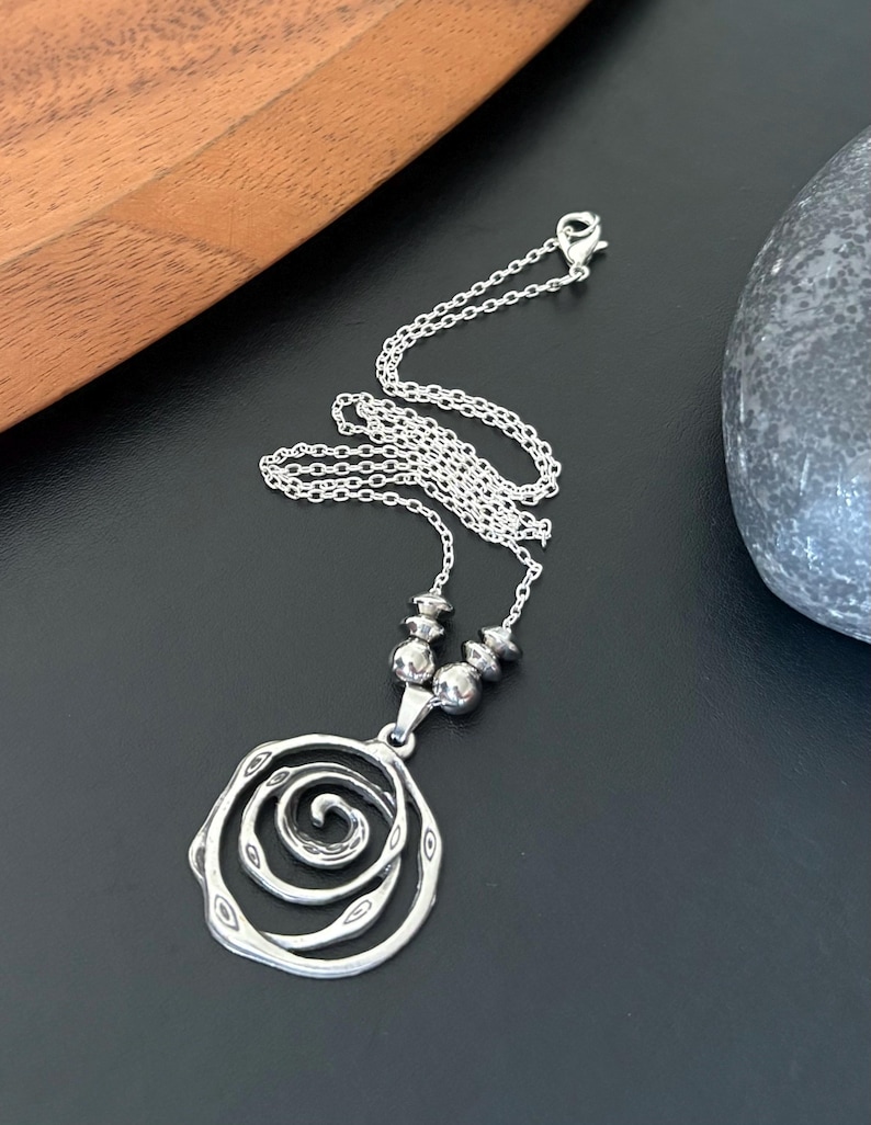 May include: A silver-toned necklace with a spiral pendant. The pendant has a layered, open design with a central spiral. The necklace chain is delicate, and the pendant is suspended from a series of small, round beads.