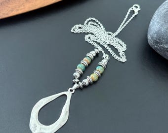 May include: Silver-toned necklace featuring a teardrop pendant and a beaded section with turquoise and tan beads. The necklace has a delicate chain and is displayed on a black surface, showcasing its intricate design.