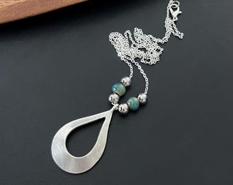 May include: A silver necklace with a teardrop-shaped pendant and green beads. The pendant has a cut-out design.