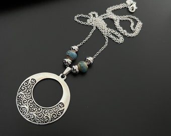 May include: A silver necklace with a large, ornate, circular pendant and blue and silver beads.