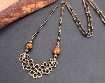 May include: A gold chain necklace with a pendant of five interconnected flower charms and two amber beads.
