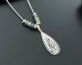 May include: A silver necklace with a teardrop-shaped pendant featuring an intricate design. The necklace is adorned with green and brown agate beads.