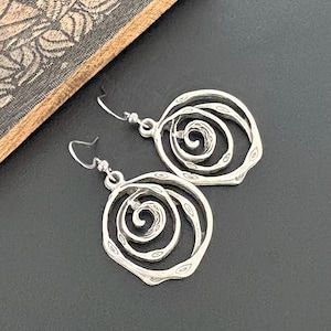 May include: A pair of silver-toned spiral earrings. Each earring features a layered, open design with a central spiral detail. The earrings have a textured, hammered appearance and are suspended from simple ear wires.