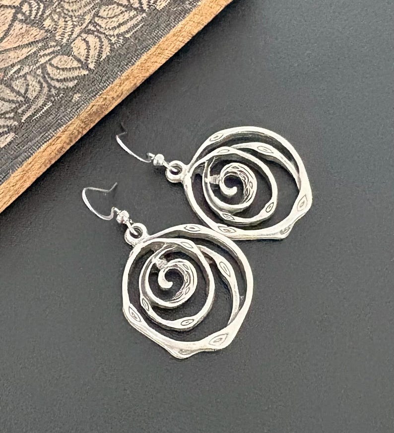 May include: A pair of silver-toned spiral earrings. Each earring features a layered, open design with a central spiral detail. The earrings have a textured, hammered appearance and are suspended from simple ear wires.