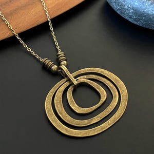 May include: A gold-toned necklace with a pendant featuring three overlapping circles. The circles are textured and have a rustic look.