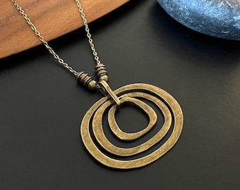May include: A gold-toned necklace with a pendant featuring three overlapping circles. The circles are textured and have a rustic look.