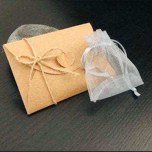 May include: A kraft paper envelope tied with twine, a small round tag, and a sheer white drawstring bag. The envelope is sealed with twine and a small round tag. The bag is made of a sheer, white fabric.