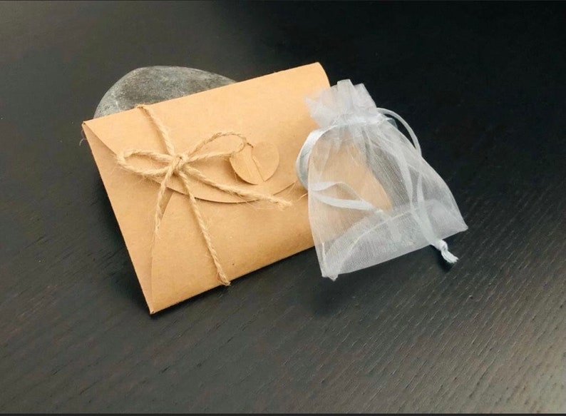 May include: A kraft paper envelope tied with twine, a small round tag, and a sheer white drawstring bag. The envelope is sealed with twine and a small round tag. The bag is made of a sheer, white fabric.