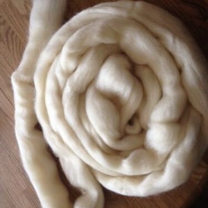 May include: A large amount of white wool roving, a type of fiber used for spinning yarn, is rolled into a tight coil.