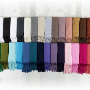 Puede incluir: Una colección de 24 bufandas de color sólido con flecos. Las bufandas están dispuestas en una fila, con los colores que van de oscuro a claro. Los colores incluyen negro, blanco, gris, beige, azul claro, marrón, rosa, dorado, burdeos, verde, azul verdoso, azul marino, morado, y más.