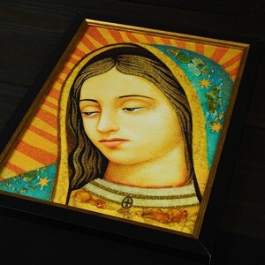 Peut inclure: Une impression artistique encadrée représentant une figure aux longs cheveux sombres, portant un voile bleu sarcelle orné d'étoiles dorées et d'embellissements texturés. Le fond présente des rayons solaires orange et jaunes dans un cadre noir.