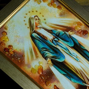 Peut inclure: Œuvre d'art religieuse encadrée représentant une femme en robe blanche et bleue, entourée d'un halo doré et de rayons de lumière. L'œuvre est ornée de pierres de couleur ambre et encadrée d'un cadre doré.