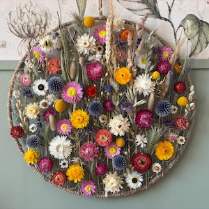 May include: A circular floral wall hanging featuring a variety of dried flowers in shades of yellow, pink, red, and white. The flowers are arranged on a woven, circular base, creating a vibrant and natural decorative piece.