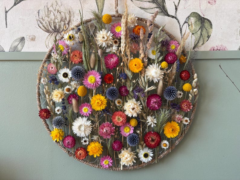 May include: A circular floral wall hanging featuring a variety of dried flowers in shades of yellow, pink, red, and white. The flowers are arranged on a woven, circular base, creating a vibrant and natural decorative piece.