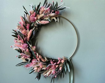 Una romantica ghirlanda primaverile adornata con foglie di ulivo ed erbe rosa. Decorazione domestica unica nel suo genere su cerchio dorato