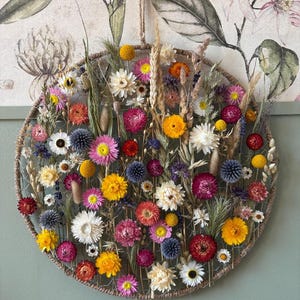 May include: A circular floral wall hanging, 40 cm in diameter, featuring a variety of dried flowers in shades of yellow, pink, orange, and white. The flowers are arranged within a woven frame, creating a natural and decorative piece. The text "40 cm diameter" is at the bottom.