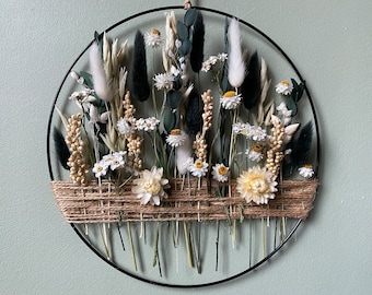 Puede incluir: Una corona de flores secas con flores blancas y crema, follaje verde y cuerda marrón. La corona se muestra en una pared verde claro.