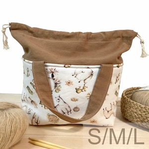 Könnte beinhalten: Eine beige-braune Tragetasche mit Kordelzugverschluss. Die Tasche hat einen weißen Stoff mit einem Wüstenmuster, einschließlich Kakteen und Lamas. Die Tasche hat braune Griffe und den Text "S/M/L" unten.