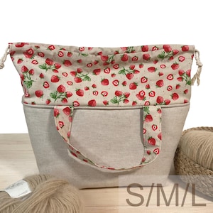 Könnte beinhalten: Beige Tragetasche mit Erdbeerdruck-Kordelzug oben und Griffen. Die Tasche hat eine rechteckige Form und ist aus einem robusten Stoff gefertigt. Der Text "S/M/L" ist unten rechts sichtbar.