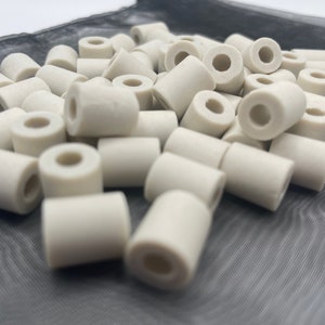 May include: A pile of white ceramic rings with a hole in the centre. The rings are arranged in a random pattern on a black mesh surface.