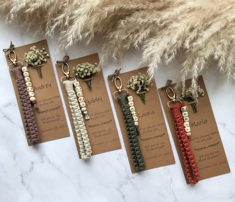 The macrame keychain is attached to the kraft card. There are white flowers on the customizable card.