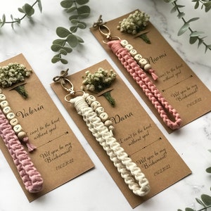 The macrame keychain is attached to the kraft card. There are white flowers on the customizable card.