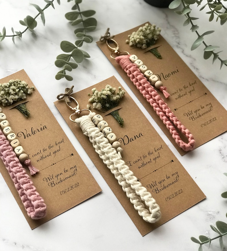 The macrame keychain is attached to the kraft card. There are white flowers on the customizable card.