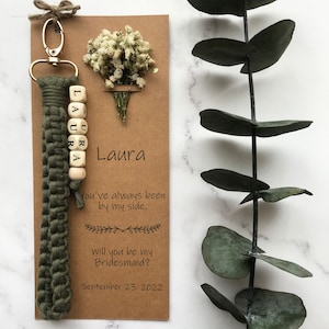 The macrame keychain is attached to the kraft card. There are white flowers on the customizable card.