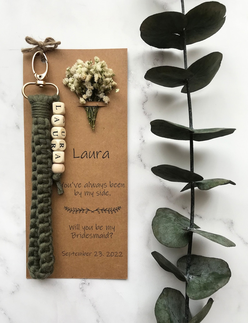 The macrame keychain is attached to the kraft card. There are white flowers on the customizable card.