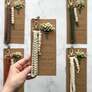 The macrame keychain is attached to the kraft card. There are white flowers on the customizable card.