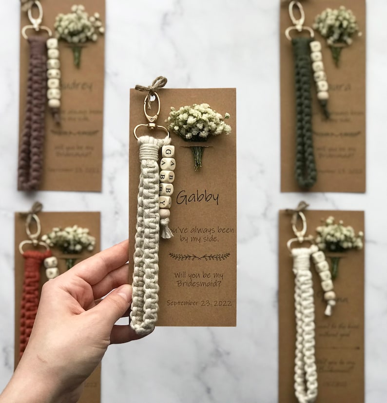 The macrame keychain is attached to the kraft card. There are white flowers on the customizable card.