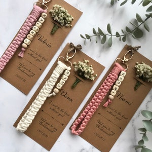 The macrame keychain is attached to the kraft card. There are white flowers on the customizable card.