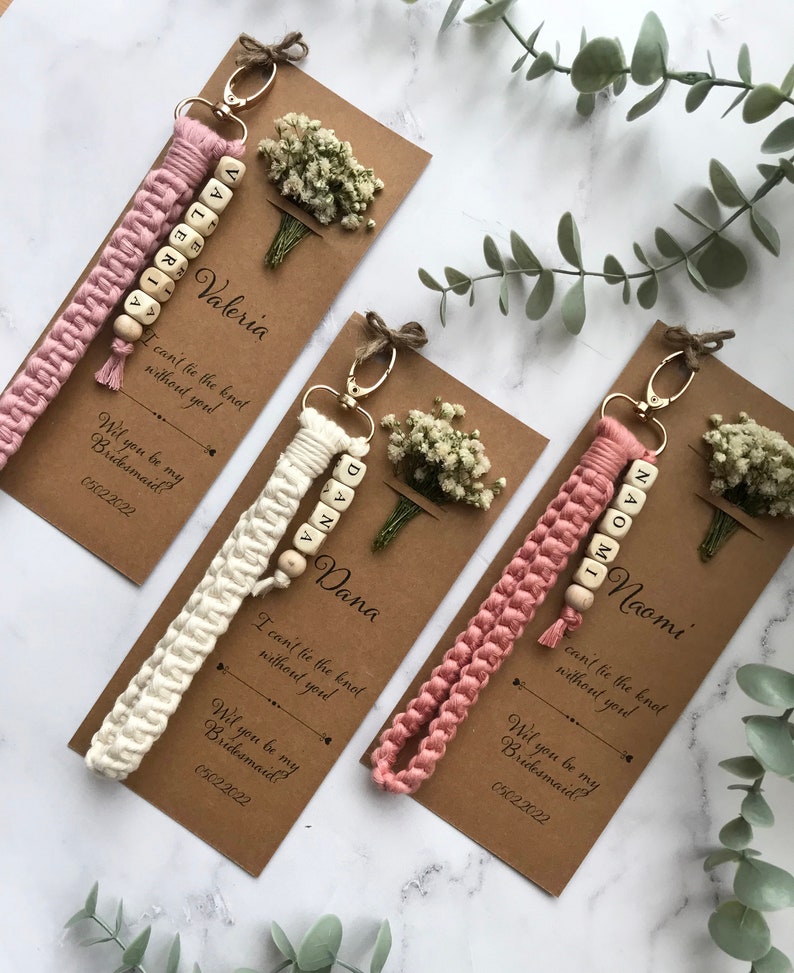The macrame keychain is attached to the kraft card. There are white flowers on the customizable card.