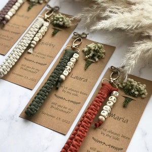 The macrame keychain is attached to the kraft card. There are white flowers on the customizable card.