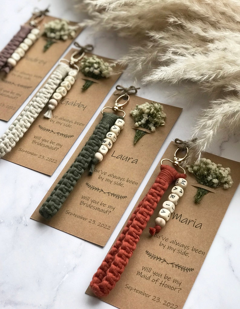 The macrame keychain is attached to the kraft card. There are white flowers on the customizable card.