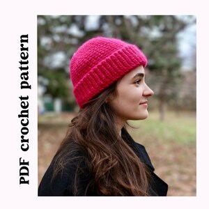 Könnte beinhalten: Nahaufnahme einer Frau, die eine leuchtend pinkfarbene Häkelmütze trägt. Die Mütze hat ein schlichtes Design und ist aus weichem Garn gefertigt.