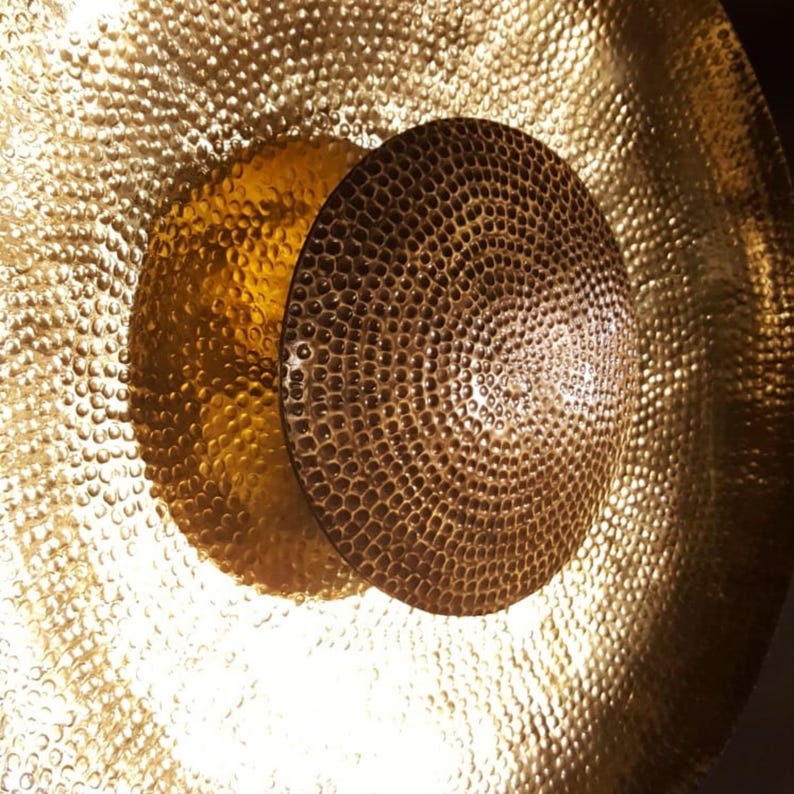 May include: A close-up shot of a golden gong with a textured surface and a smaller, darker brown disc in the centre. The gong's hammered texture creates a reflective surface. The lighting accentuates the metallic sheen and intricate details.