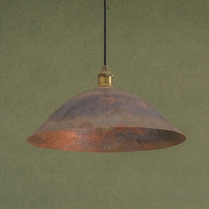 May include: A hanging pendant light with a copper-colored, bowl-shaped shade. The shade has a dark, mottled finish with hints of brown and rust. The fixture includes a brass-colored fitting and a black cord.