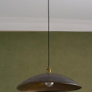 May include: A pendant light fixture with a dark brown, bowl-shaped shade and a gold-colored interior. The light hangs from a black cord attached to a gold-colored ceiling mount. The light bulb is visible.