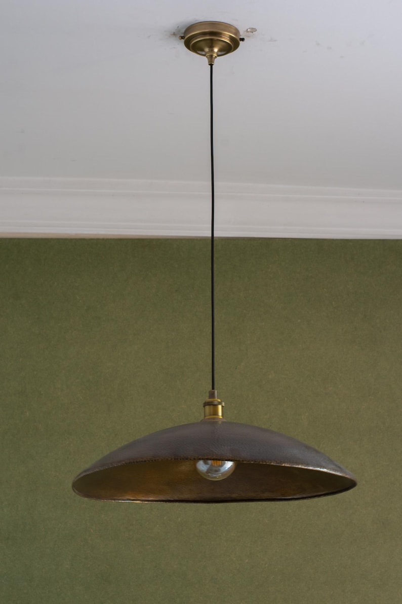 May include: A pendant light fixture with a dark brown, bowl-shaped shade and a gold-colored interior. The light hangs from a black cord attached to a gold-colored ceiling mount. The light bulb is visible.