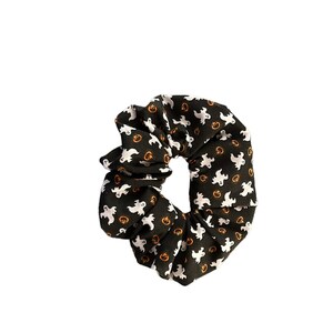 Op de afbeelding: Een zwarte scrunchie met een wit spook en oranje pompoenpatroon.